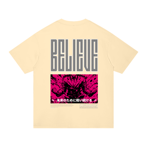 A pale cream-colored short-sleeve t-shirt shown from the back, featuring a large graphic print. The top portion displays the word 'BELIEVE' in a stylized dark gray block font, and the bottom portion features a vibrant hot pink graphic of a wolf with Japanese text underneath.