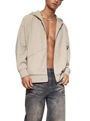 Man wearing a beige hoodie and gray jeans on a white background