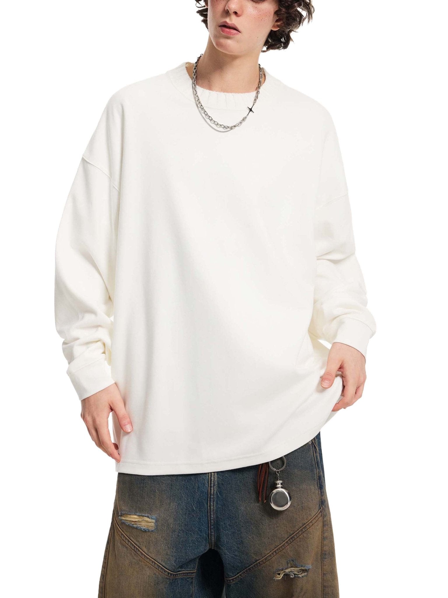 Person wearing a white oversized sweatshirt and dark jeans on a white background