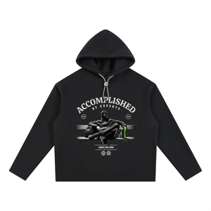 A black long-sleeve cropped hoodie with a graphic print on the front. The graphic features the text 'ACCOMPLISHED BY EXPERTS' in white arched lettering above an illustration of a person in a black suit holding a green bottle, set against a clean white background.
