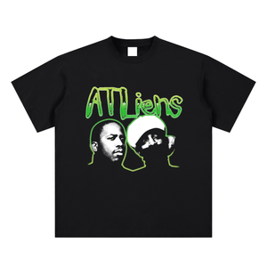 Black t-shirt with green graphic design featuring two faces and 'ATLiens' text on a white background