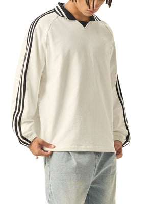 Person wearing a beige long-sleeve shirt with black stripes on sleeves and collar, paired with light gray pants.