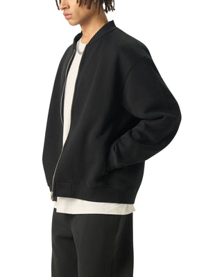 Person wearing a black bomber jacket with white trim on a white background