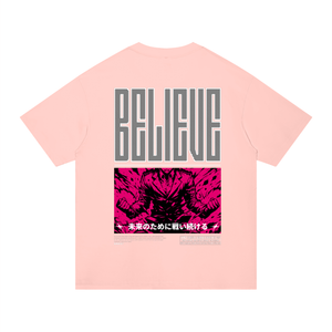 A light pink short-sleeve t-shirt shown flat against a white background, featuring a large graphic print on the back with the word 'BELIEVE' in gray block letters above a vibrant hot pink graphic panel with Japanese text.