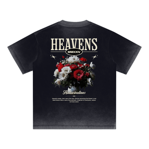A black short-sleeve t-shirt with a distressed acid-wash finish, featuring a large graphic print on the back. The graphic displays the word 'HEAVENS' in a distressed cream font, 'MMXXXIV' below it, and a colorful bouquet of red, white, and black flowers.