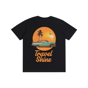 A black short-sleeve t-shirt with a retro-style graphic on the front. The graphic features a teal vintage car driving in front of a large orange sun with a palm tree silhouette, above the text 'Travel Shine' in orange script.