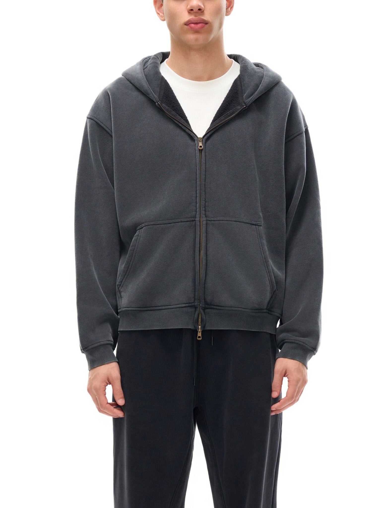 Person wearing a gray hoodie and black pants on a white background