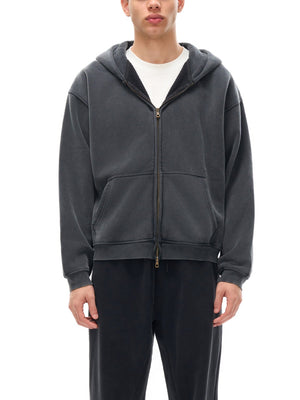 Person wearing a gray hoodie and black pants on a white background